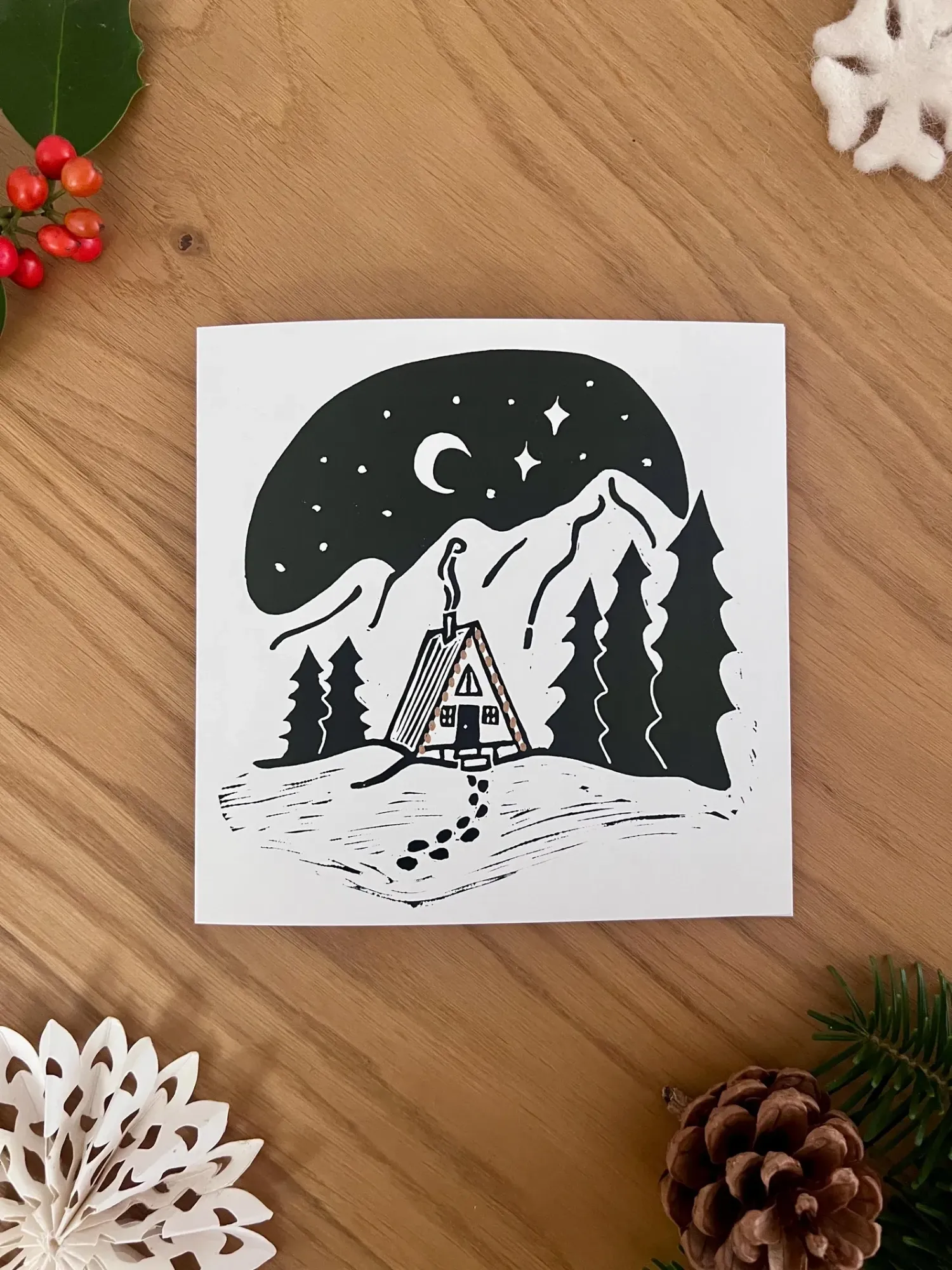 An A-frame cabin with string lights between tall fir trees, under a crescent moon