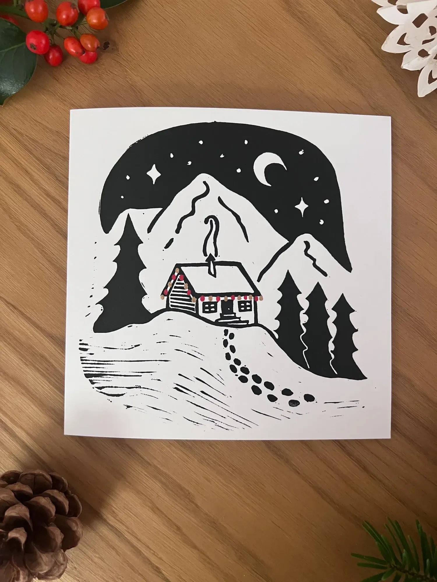 A cabin on a hilltop strung with red lights, a trail of footsteps winding down the slope