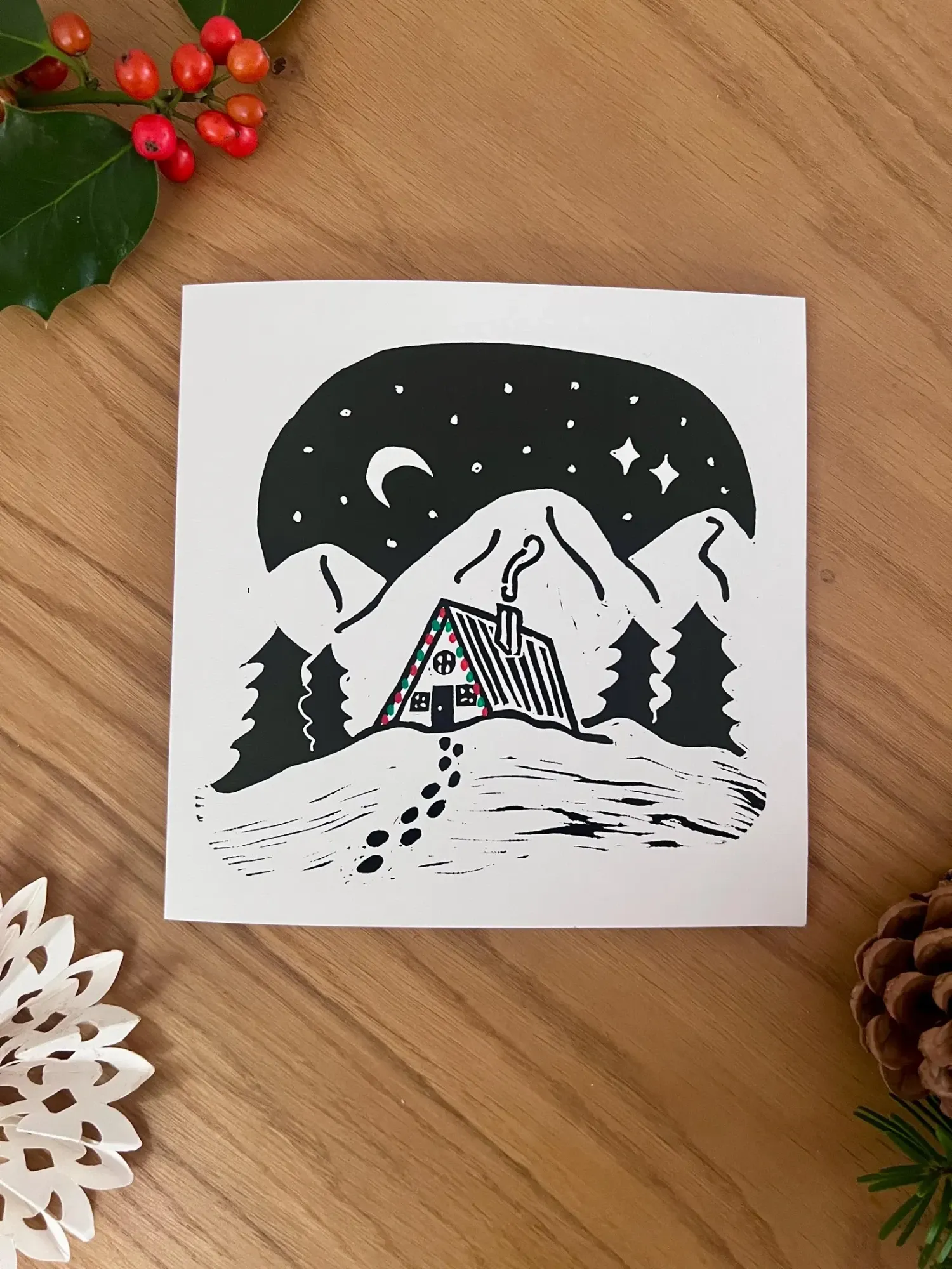 A tall A-frame cabin edged with red and green lights, nestled between pine trees