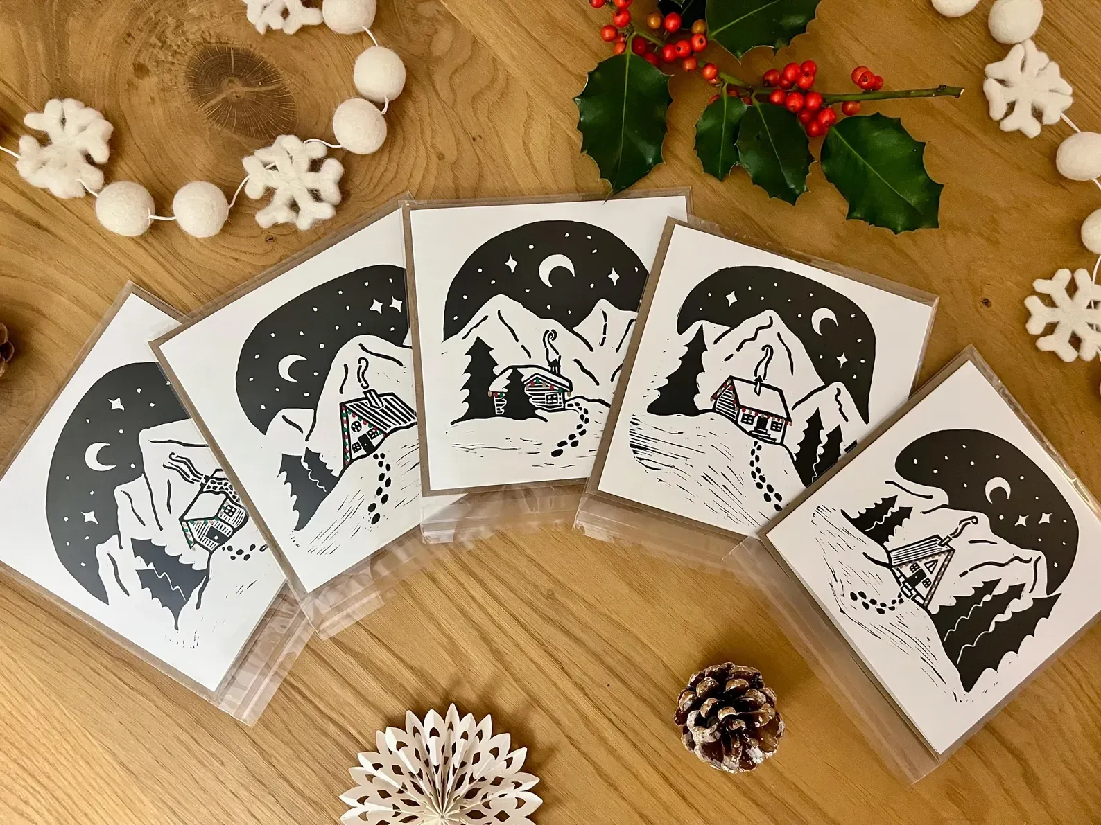 The five cards in their clear sleeves, fanned out on a wooden table with holly and felt snowflakes