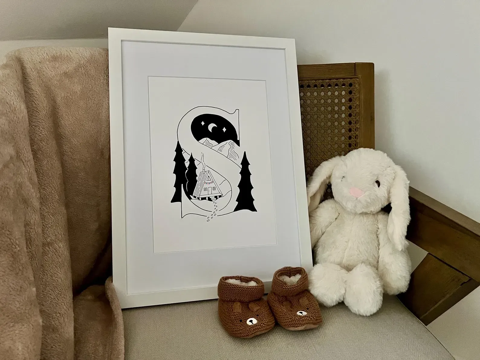 The framed letter S in a nursery, next to a toy bunny and a pair of knitted baby booties